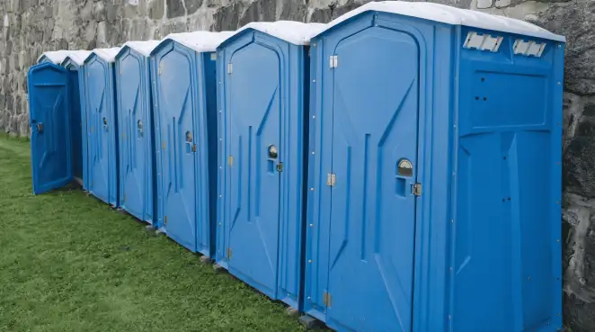 Row of blue portable toilets lined up on grass against a stone wall for event sanitation in Cedar Rapids, IA