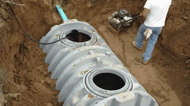 Septic tank installation showing a technician compacting soil around a new poly septic tank in an excavation pit in Cedar Rapids, IA